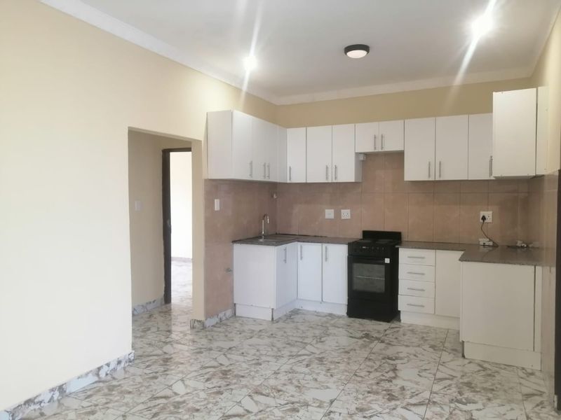 A clean, functional kitchen featuring white cabinetry, granite countertops, tiled backsplash, and a freestanding stove, set against neutral walls and tiled flooring.
