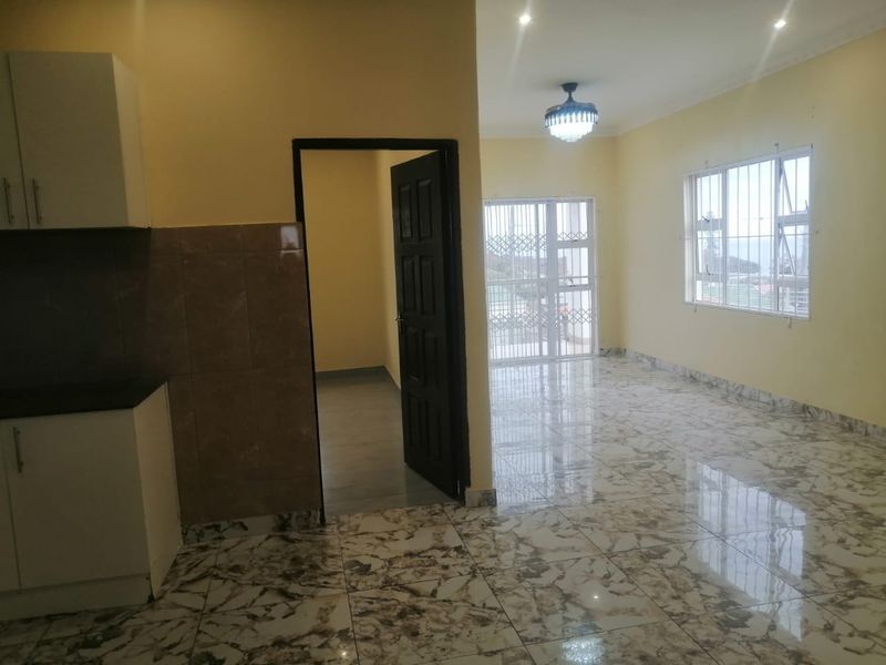 An open-plan living and kitchen area featuring polished marble-look floor tiles, neutral walls, and secure window and door access.