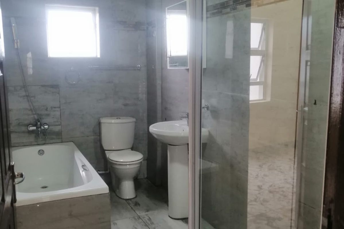Modern bathroom featuring a bathtub, pedestal basin, toilet, and a separate glass-enclosed shower with contemporary grey tiling throughout.