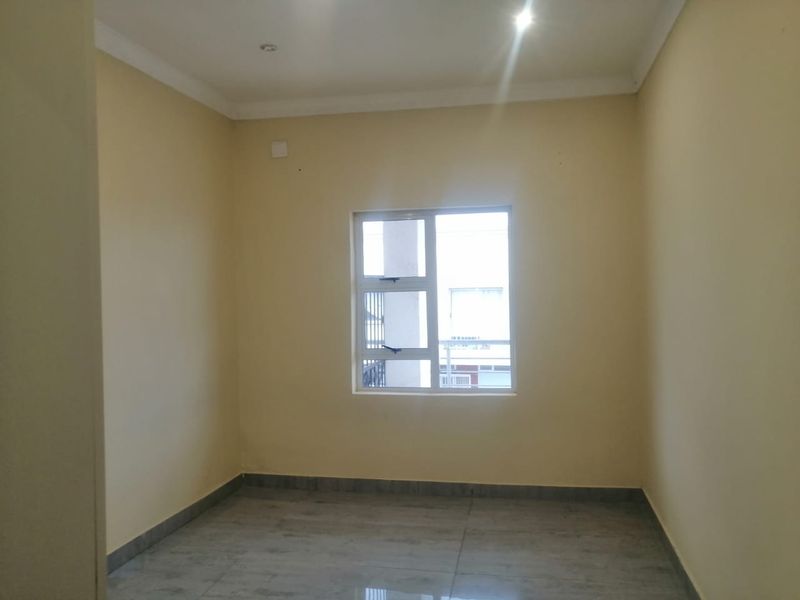 A vacant bedroom featuring neutral wall paint, tiled flooring, and an aluminium window frame, offering a clean and blank canvas for personalization.