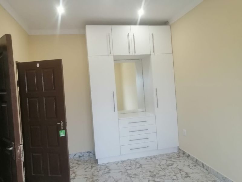 A clean bedroom featuring a modern white built-in wardrobe with an integrated vanity mirror and tiled flooring.