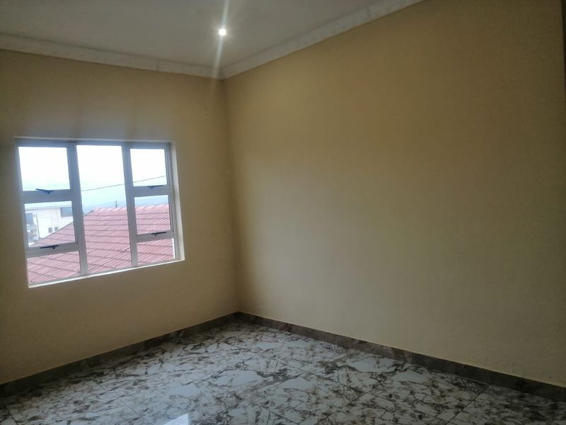 An empty bedroom featuring tiled flooring, neutral walls, and a window with natural light.