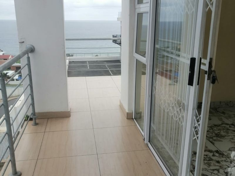 A spacious balcony featuring tiled flooring, a metal balustrade, and sliding glass doors with security gates, offering an open outdoor area.