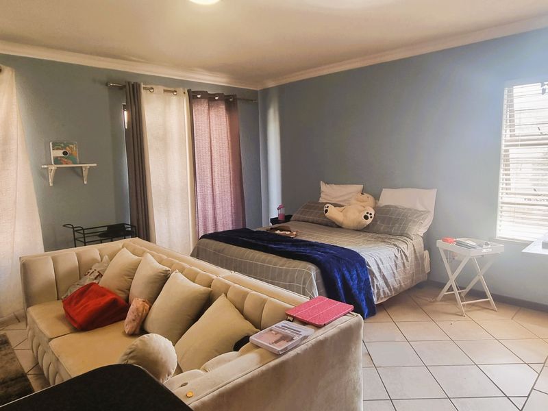 Spacious bedroom featuring tiled flooring, neutral wall tones, and natural light through large windows.