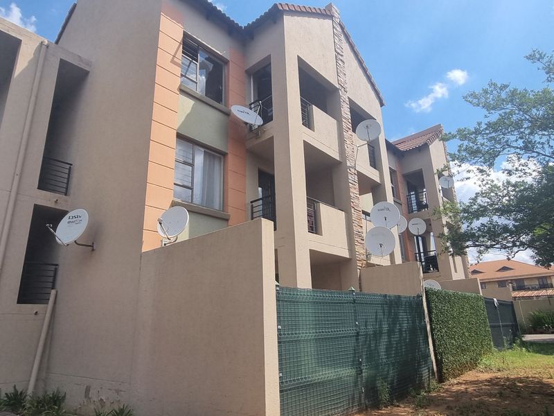 Exterior view of a multi-story apartment complex featuring balconies, satellite dish installations, and a combination of stucco and stone facade finishes.