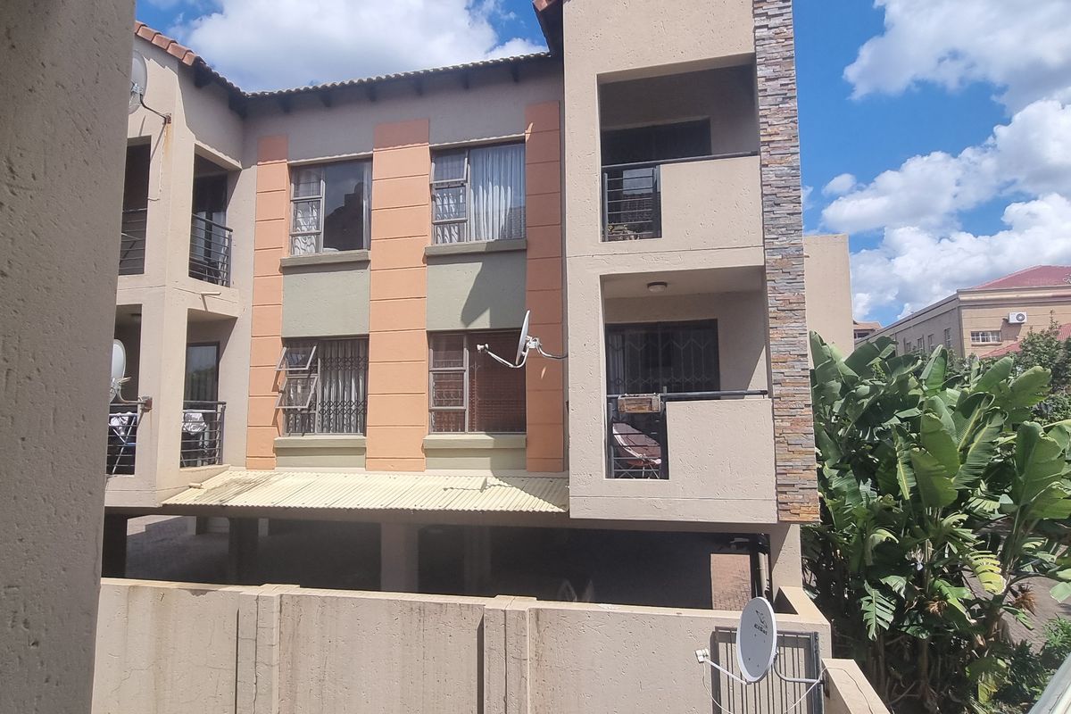 Rear elevation of a multi-story apartment complex featuring balconies with security bars, stone cladding accents, and a tiled roof.