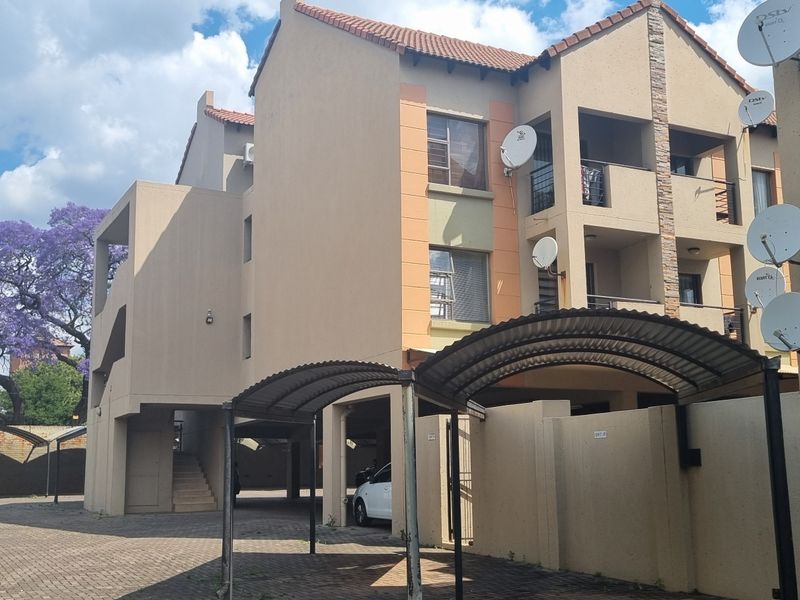 Exterior view of an apartment complex featuring covered parking bays, multi-level balconies, and a paved driveway area.