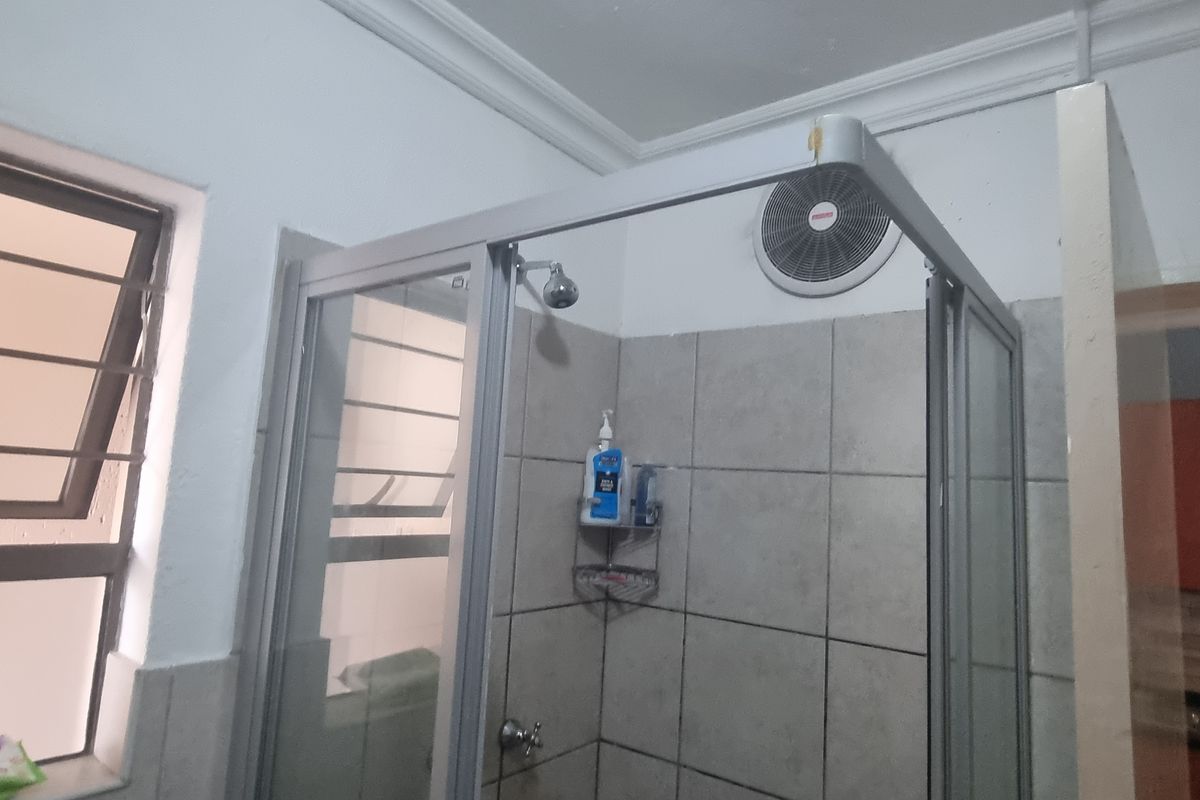 A functional bathroom featuring a shower enclosure with tiled walls, an extractor fan, and a louvered window for ventilation.