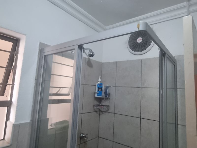 A functional bathroom featuring a shower enclosure with tiled walls, an extractor fan, and a louvered window for ventilation.