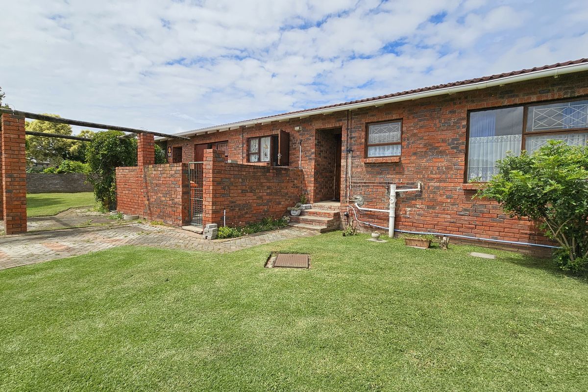 Rear view of a face brick townhouse featuring a paved patio area, a brick pergola structure, and a well-maintained lawn garden.