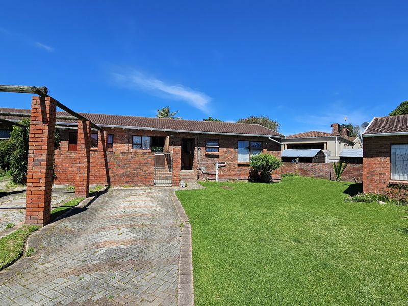 Rear view of a brick townhouse featuring a paved driveway, pergola structure, and a well-maintained lawn area.