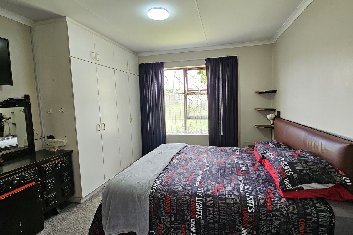 A functional bedroom featuring built-in cupboards, a window with security bars, and wall-mounted shelving, providing practical storage and natural light.