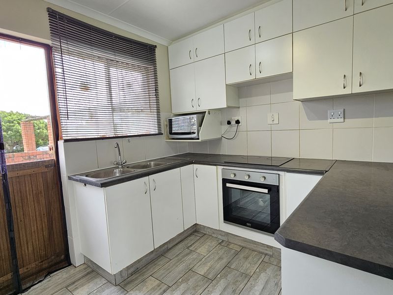 A functional kitchen featuring white built-in cabinetry, dark laminate countertops, a built-in oven with electric hob, and tiled flooring.