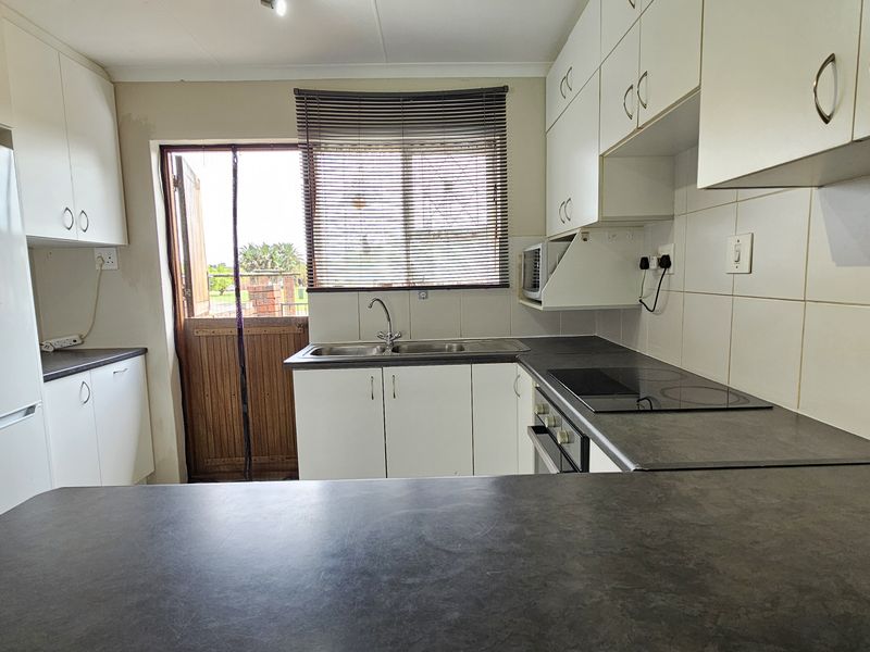 Functional kitchen featuring white cabinetry, dark laminate countertops, built-in oven and hob, and a tiled backsplash with direct access to the exterior.