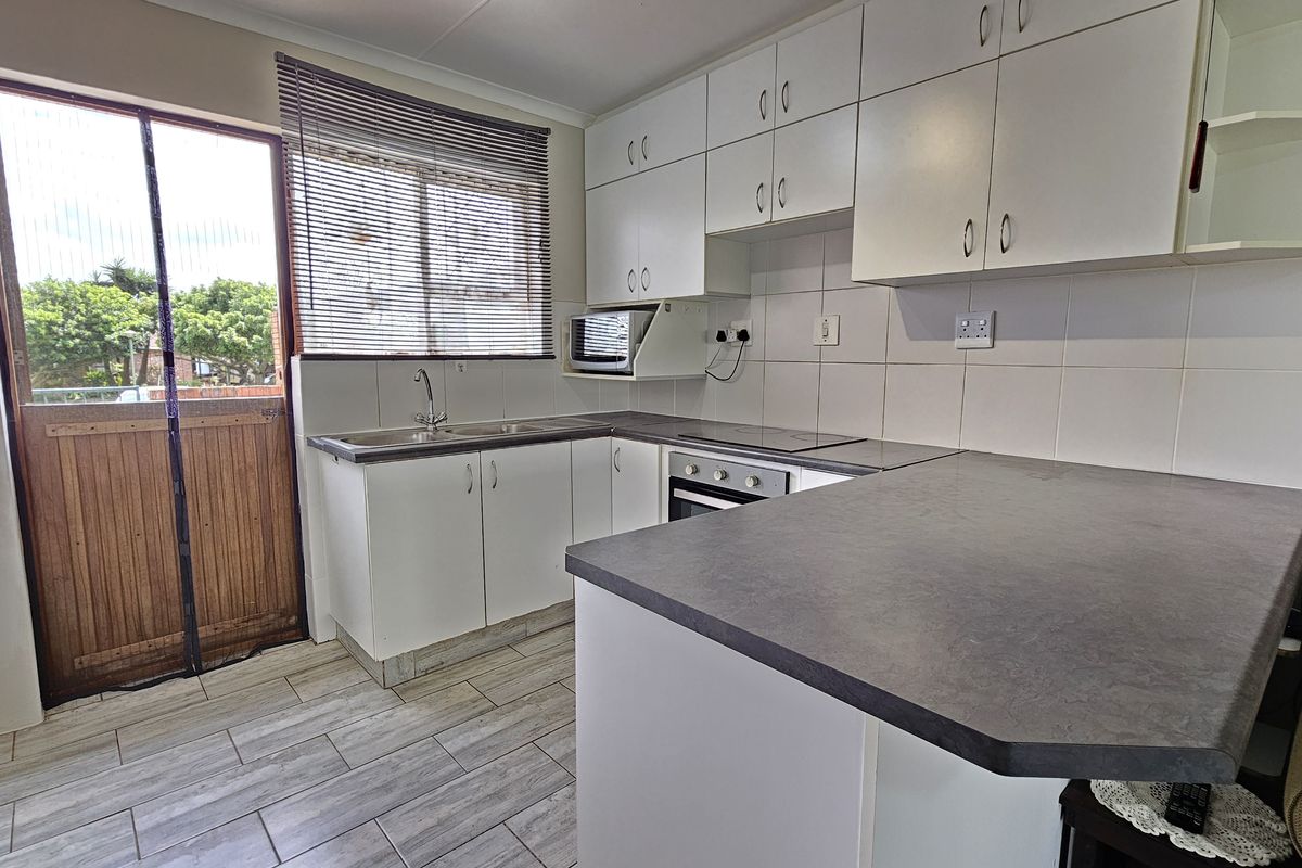 A functional kitchen featuring white cabinetry, dark laminate countertops, built-in oven and hob, tiled backsplash, and direct access to the exterior.