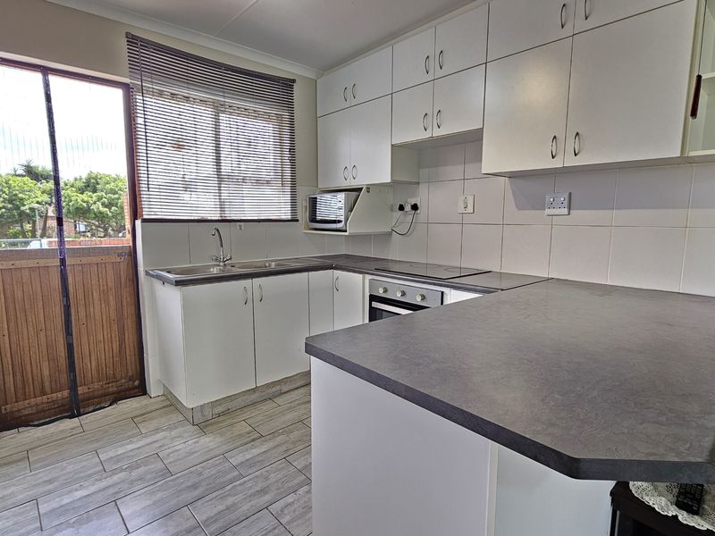 A functional kitchen featuring white cabinetry, dark laminate countertops, built-in oven and hob, tiled backsplash, and direct access to the exterior.