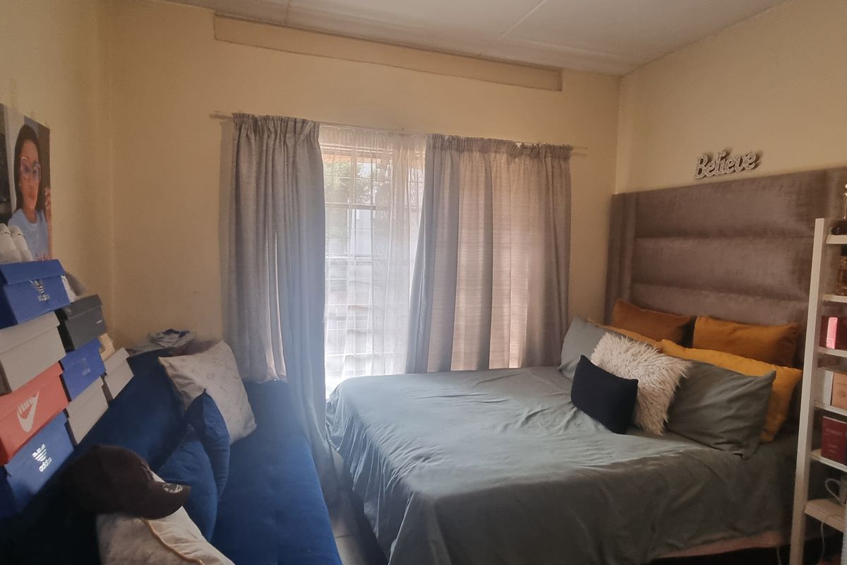 A bedroom featuring a window with curtains and visible wear on the wall surfaces.