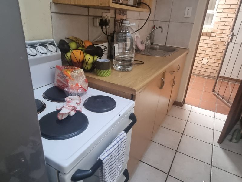 A compact kitchen featuring tiled flooring, built-in cabinetry, a stainless steel sink, and a freestanding stove, requiring cosmetic updates to improve its overall condition.