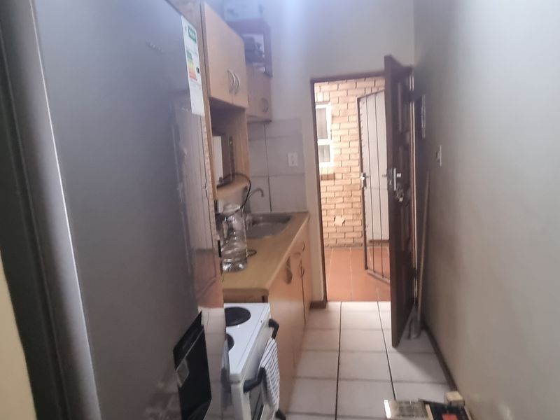 A compact kitchen featuring built-in cabinetry, tiled flooring, and direct access to an exterior area through a security gate.