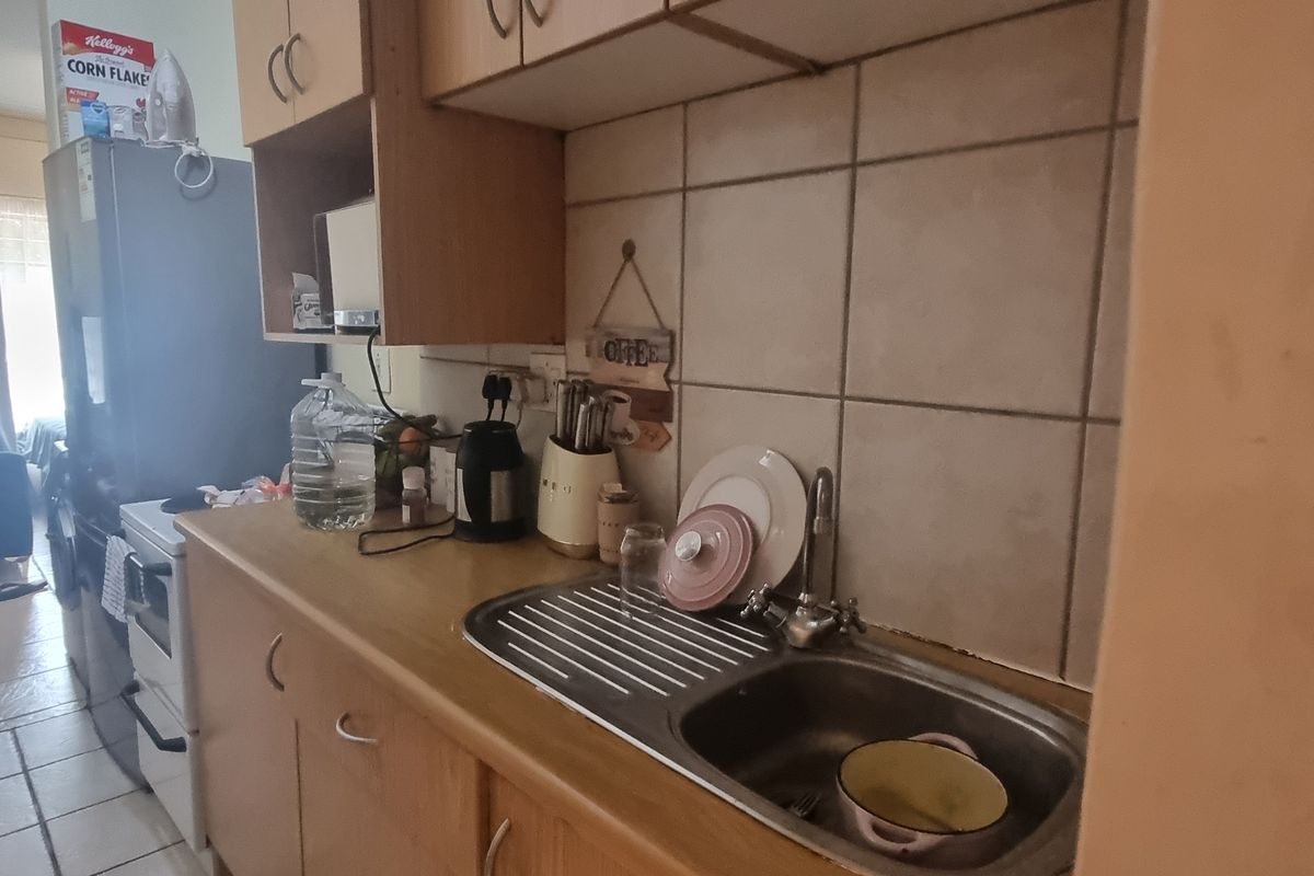 A compact kitchen featuring laminate countertops, a stainless steel sink, tiled backsplash, and built-in cabinetry, requiring cosmetic updates to modernize the space.
