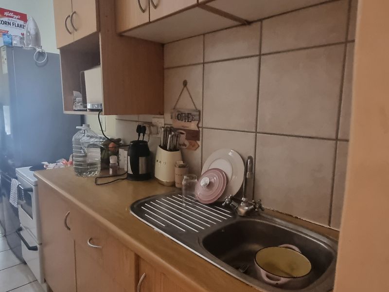 A compact kitchen featuring laminate countertops, a stainless steel sink, tiled backsplash, and built-in cabinetry, requiring cosmetic updates to modernize the space.
