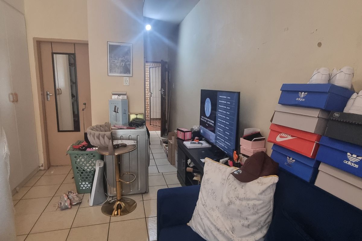 A living area featuring tiled flooring and a built-in cupboard, currently cluttered with personal items and in need of cosmetic wall repairs.