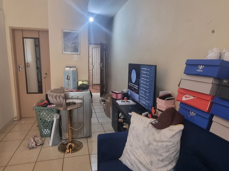 A living area featuring tiled flooring and a built-in cupboard, currently cluttered with personal items and in need of cosmetic wall repairs.