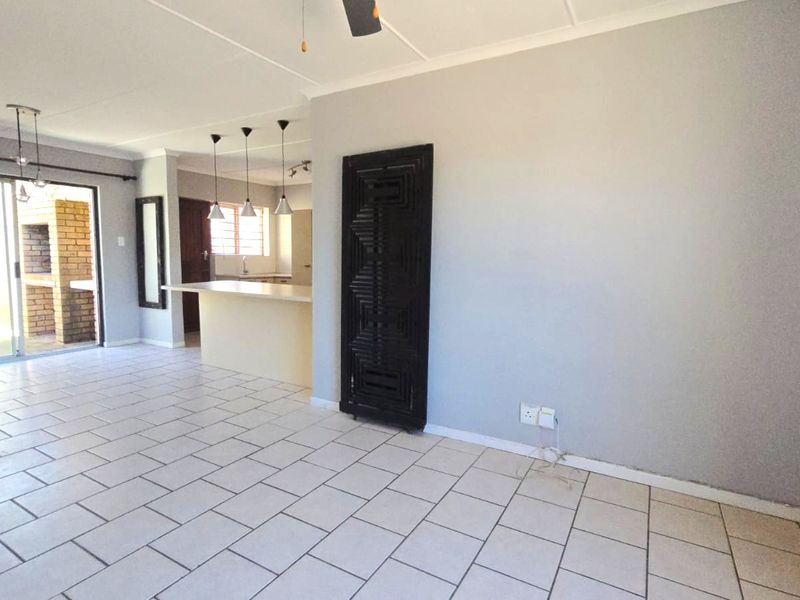 Spacious open-plan living area featuring ceramic tile flooring, a breakfast bar, and direct access to an outdoor patio with a built-in brick braai.