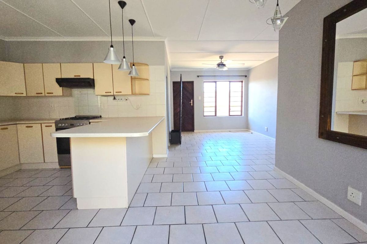 Spacious open-plan living and kitchen area featuring tiled flooring, neutral cabinetry, and a breakfast island, offering a versatile layout for modern living.