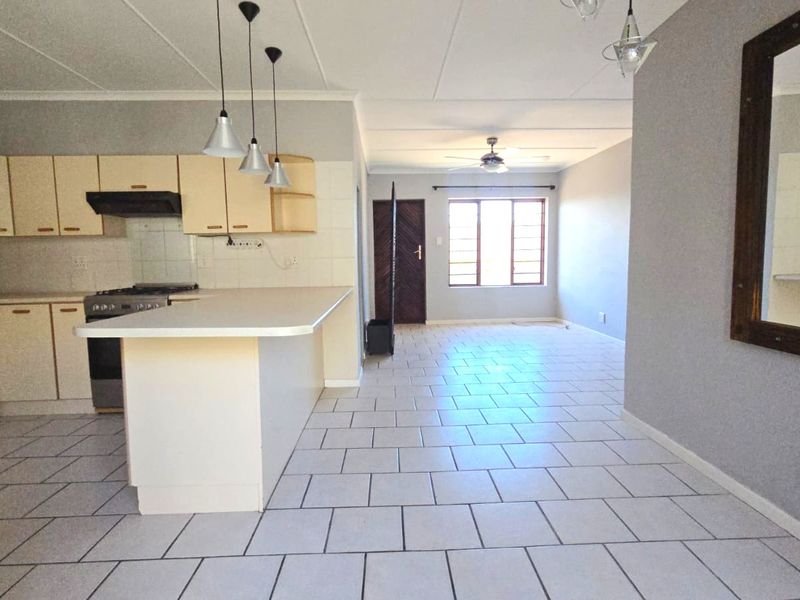 Spacious open-plan living and kitchen area featuring tiled flooring, neutral cabinetry, and a breakfast island, offering a versatile layout for modern living.