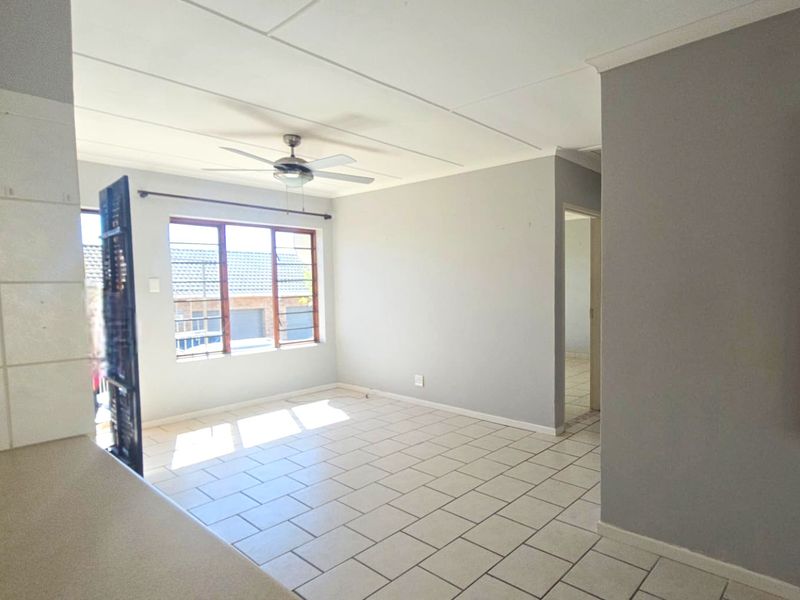An open-plan living area featuring neutral grey walls, tiled flooring, and a ceiling fan, offering a bright and versatile space.