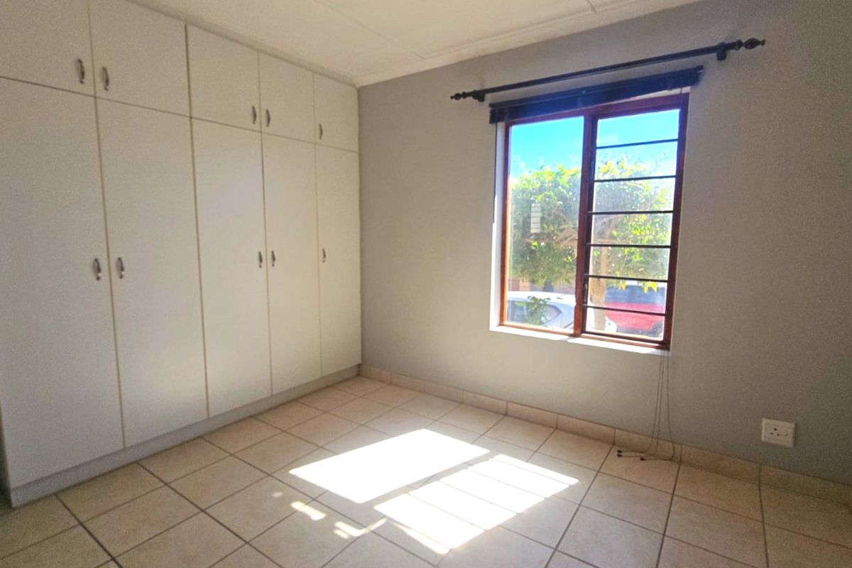 A bright, empty bedroom featuring neutral tiled flooring and extensive built-in cupboard storage, offering a clean and versatile space.