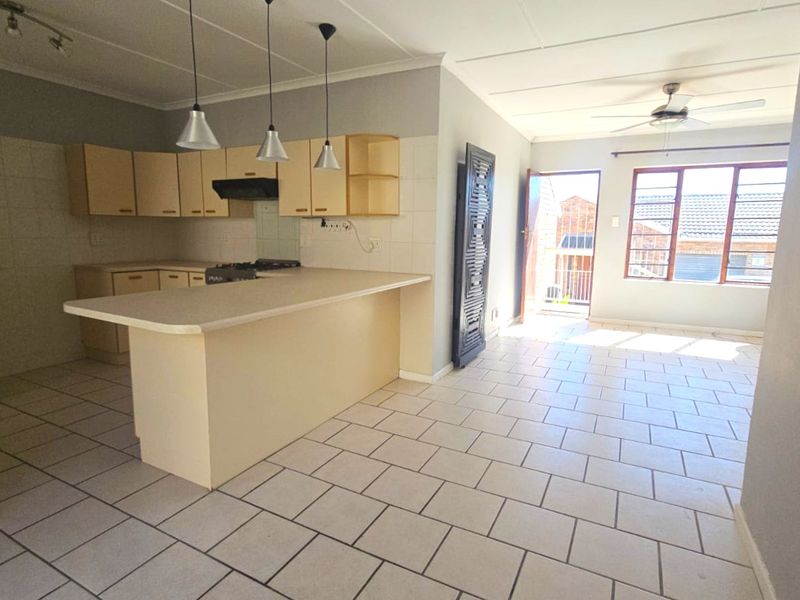 Open-plan kitchen and living area featuring tiled flooring, built-in cabinetry, a breakfast island, and a ceiling fan, offering a functional layout.