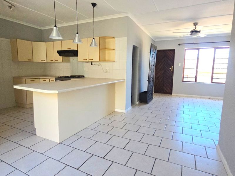 Open-plan kitchen and living area featuring tiled flooring, neutral cabinetry, a breakfast bar, and a ceiling fan in a bright, spacious layout.
