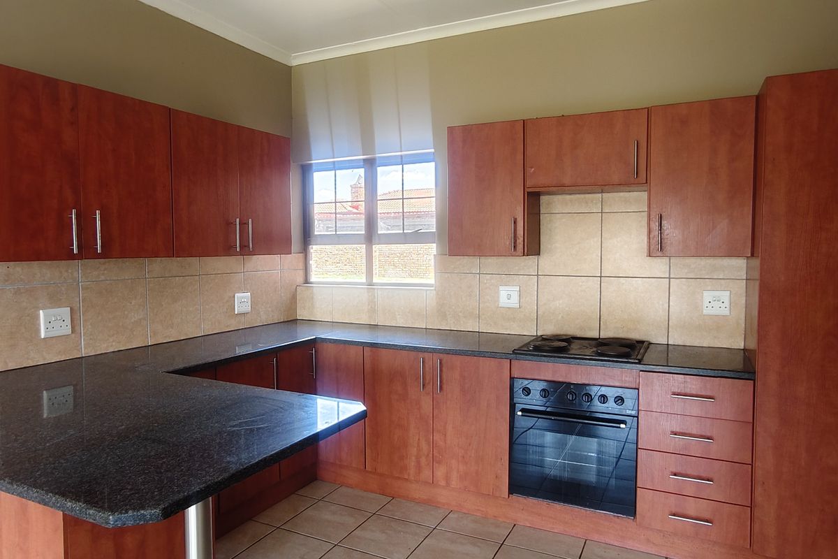 A functional kitchen featuring granite countertops, laminate cabinetry, a built-in oven, and an electric hob with a breakfast bar area.