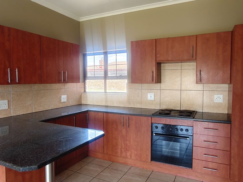 A functional kitchen featuring granite countertops, laminate cabinetry, a built-in oven, and an electric hob with a breakfast bar area.