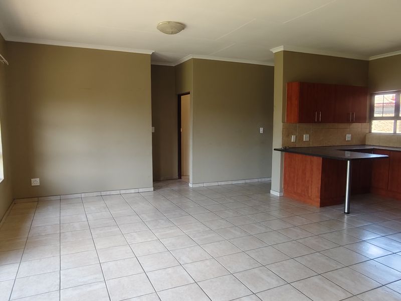 Spacious open-plan living and kitchen area featuring tiled floors, wooden cabinetry, and direct access to the exterior through a sliding glass door.