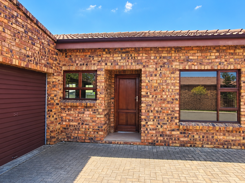 Front elevation of a face brick house featuring a paved driveway, single garage, and timber entrance door with aluminium window frames.
