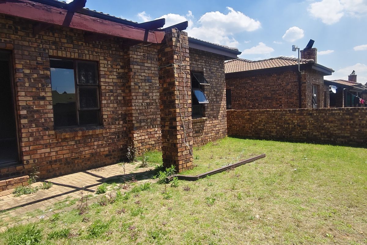 Rear view of a face brick house featuring a paved patio area, timber pergola, and a private garden enclosed by a brick boundary wall.
