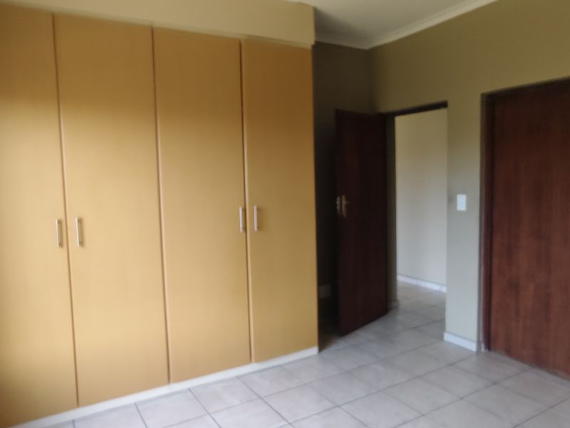 A spacious bedroom featuring built-in cupboards, tiled flooring, and neutral wall finishes, offering a clean and functional living space.