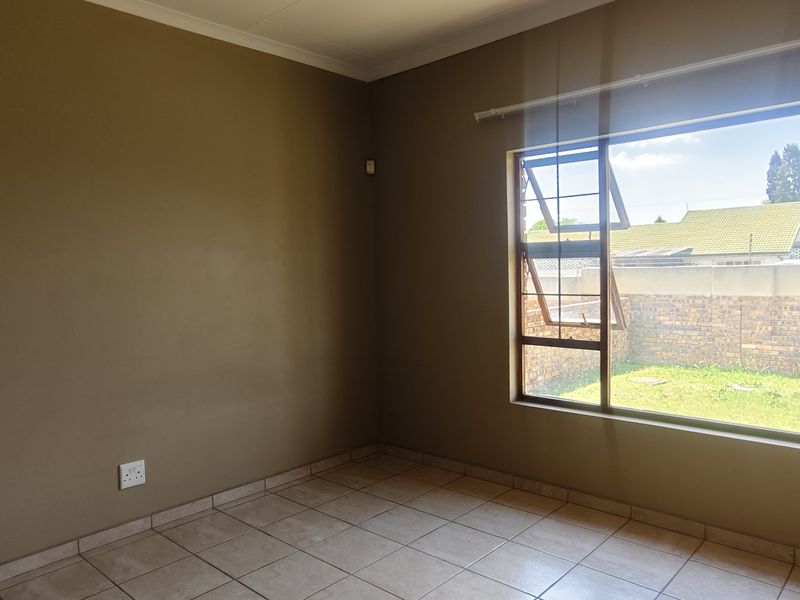 A vacant bedroom featuring neutral wall paint, tiled flooring, and a large window providing natural light and views of the rear garden.