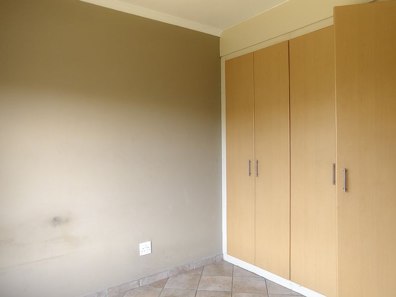 A vacant bedroom featuring built-in wooden cupboards and tiled flooring, requiring minor cosmetic updates to the wall finishes.