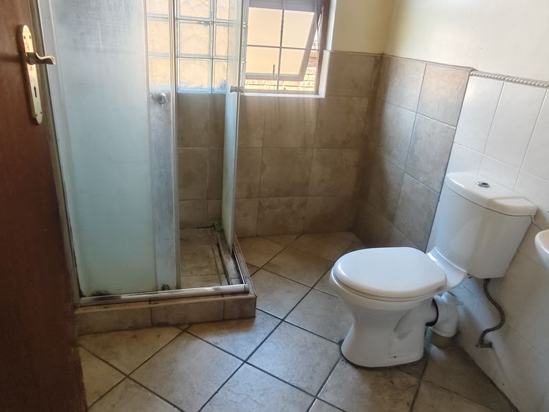 A functional bathroom featuring a shower enclosure, pedestal basin, and toilet, finished with ceramic floor and wall tiling.