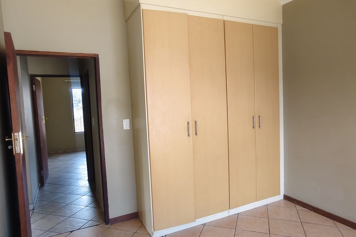 A vacant bedroom featuring built-in wooden cupboards and tiled flooring, with a view into the adjacent hallway.