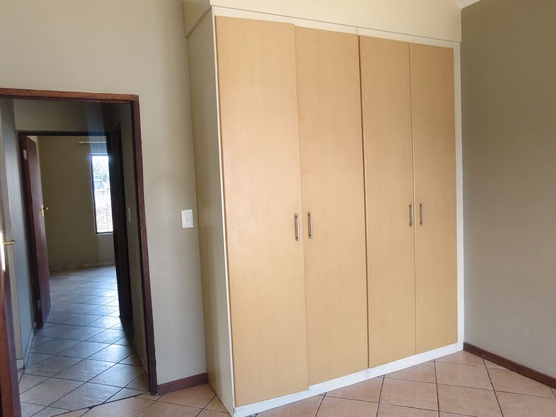 A vacant bedroom featuring built-in wooden cupboards and tiled flooring, with a view into the adjacent hallway.