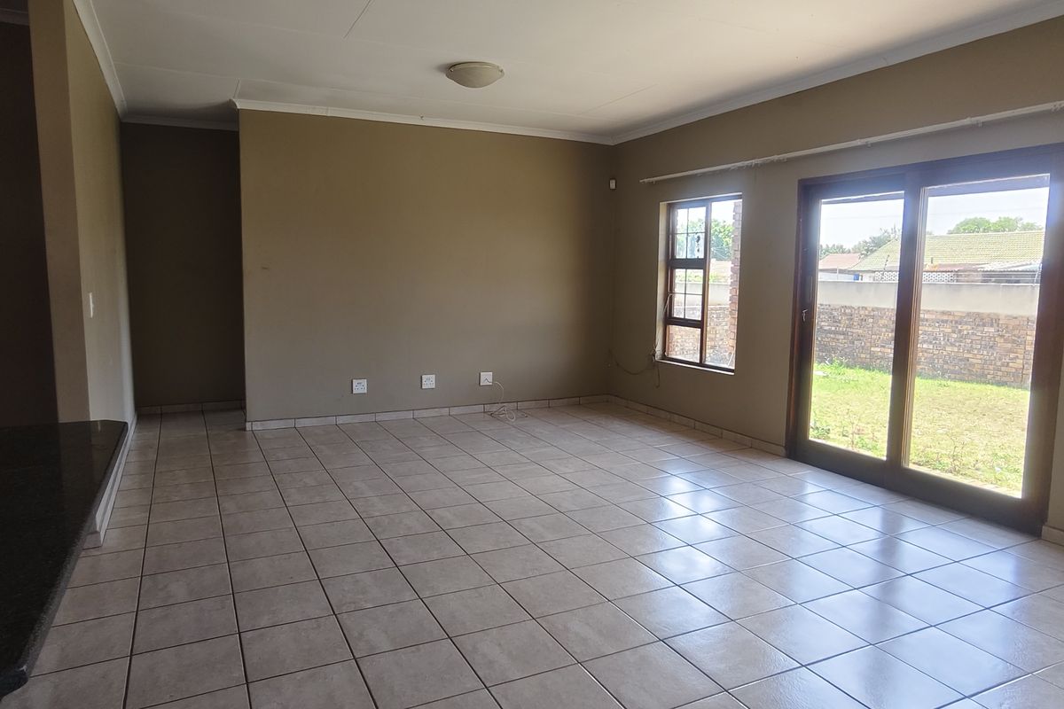 Spacious, empty living area featuring neutral tiled flooring, large windows, and sliding glass doors providing direct access to the garden.