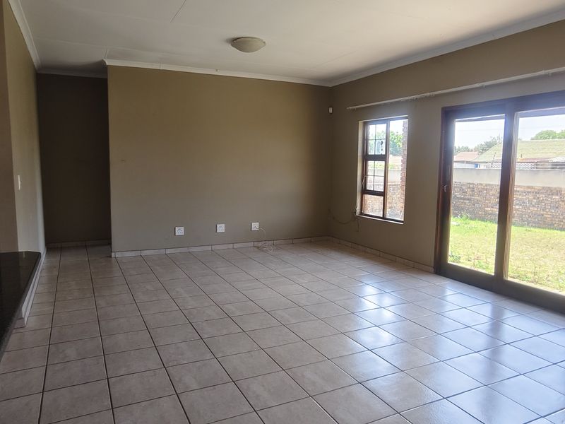 Spacious, empty living area featuring neutral tiled flooring, large windows, and sliding glass doors providing direct access to the garden.