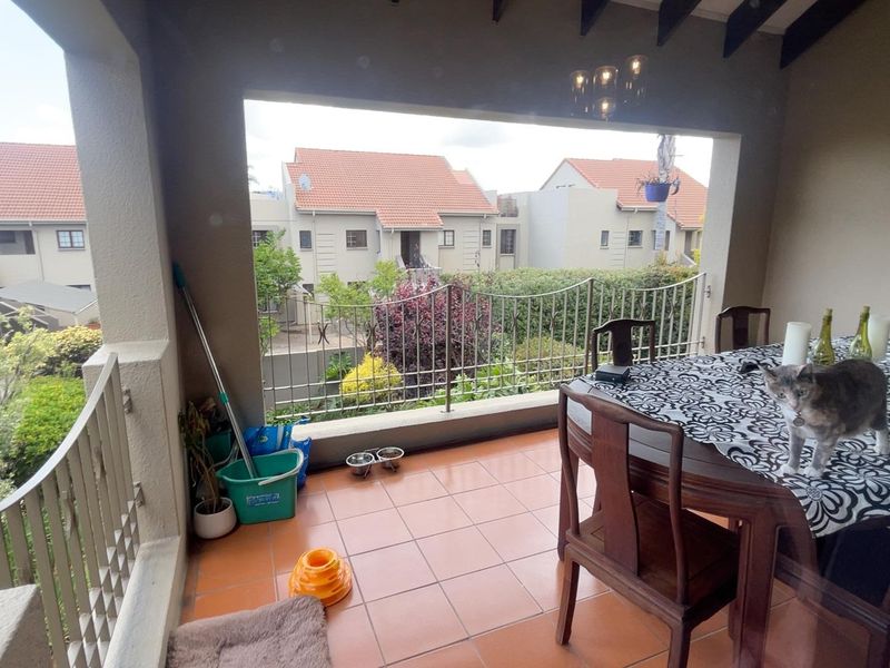 A covered balcony featuring tiled flooring and a metal balustrade, offering an elevated view of the surrounding townhouse complex.