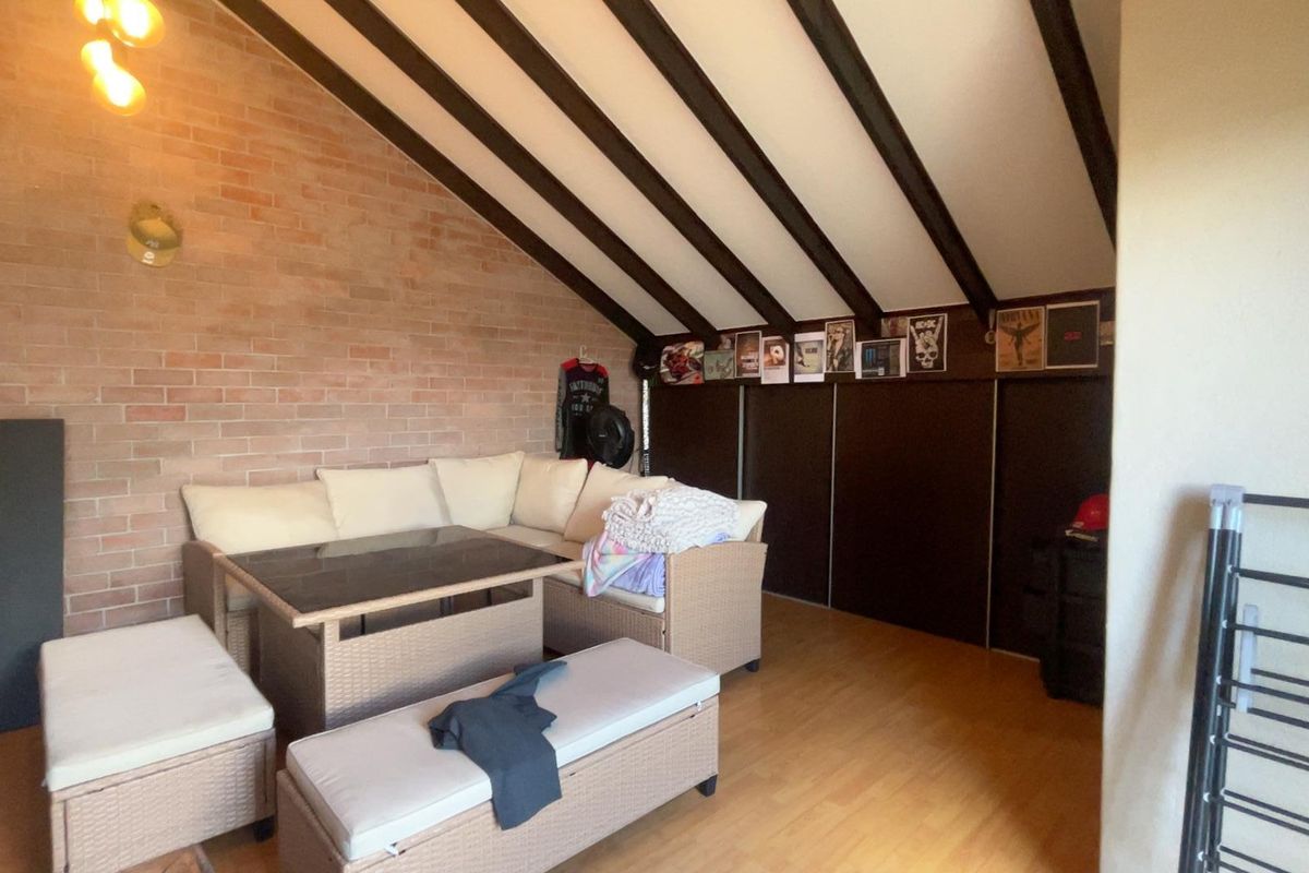 A living room featuring exposed brick walls, vaulted ceilings with timber beams, and built-in storage, offering a rustic and character-filled living space.
