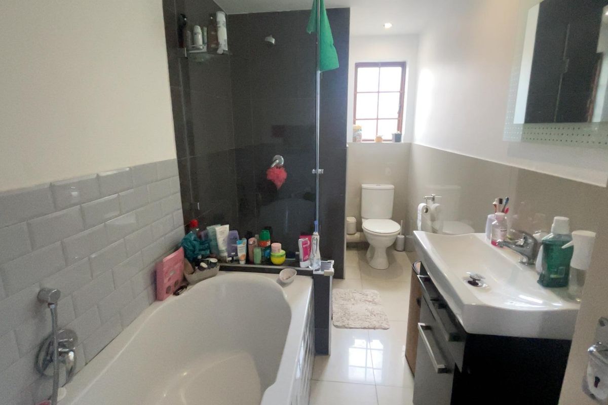 A functional bathroom featuring a bathtub, separate shower area with dark tiling, a modern vanity basin, and a toilet.